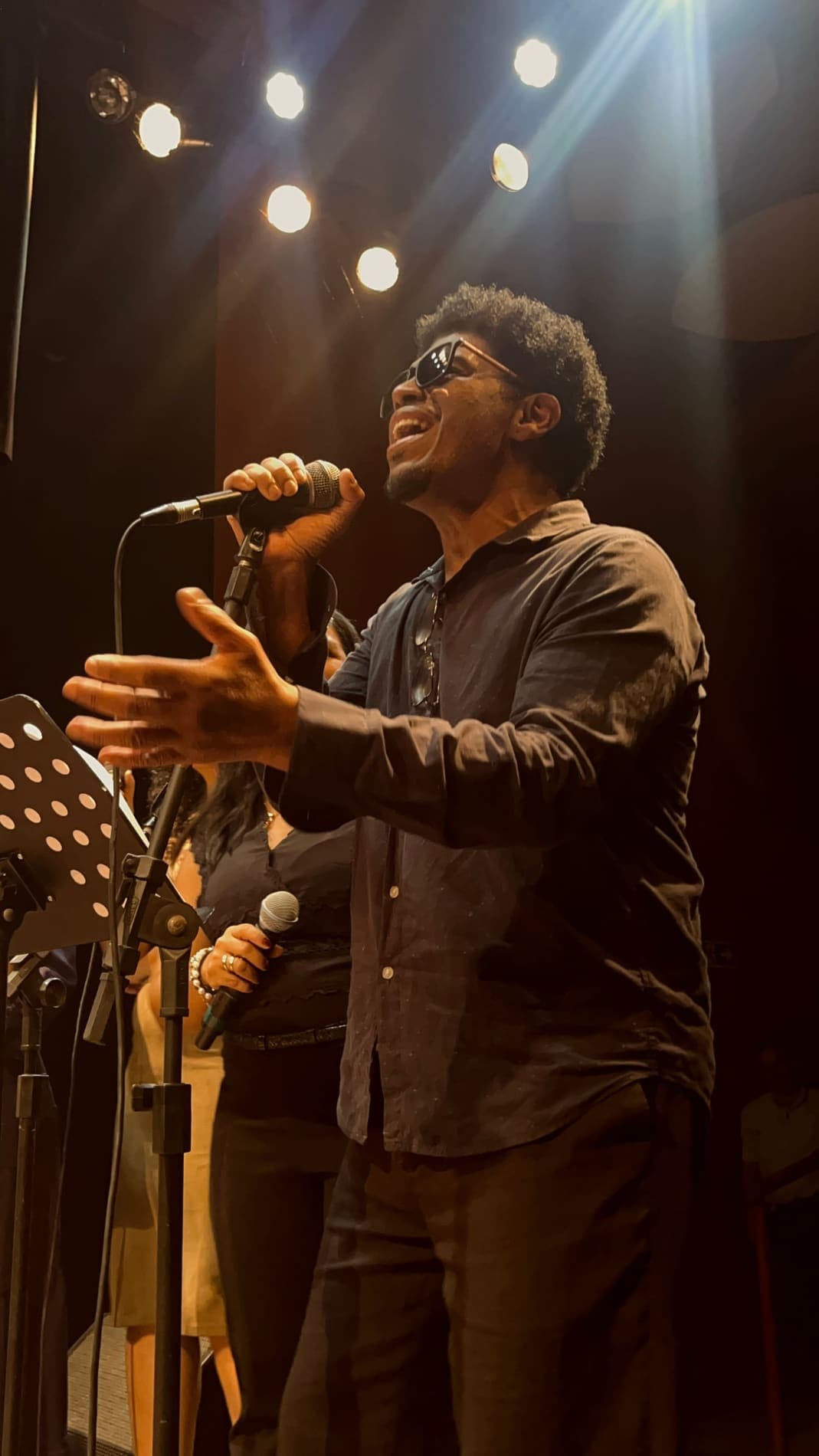 Cantor de braços abertos no microfone, sob a luz quente do palco